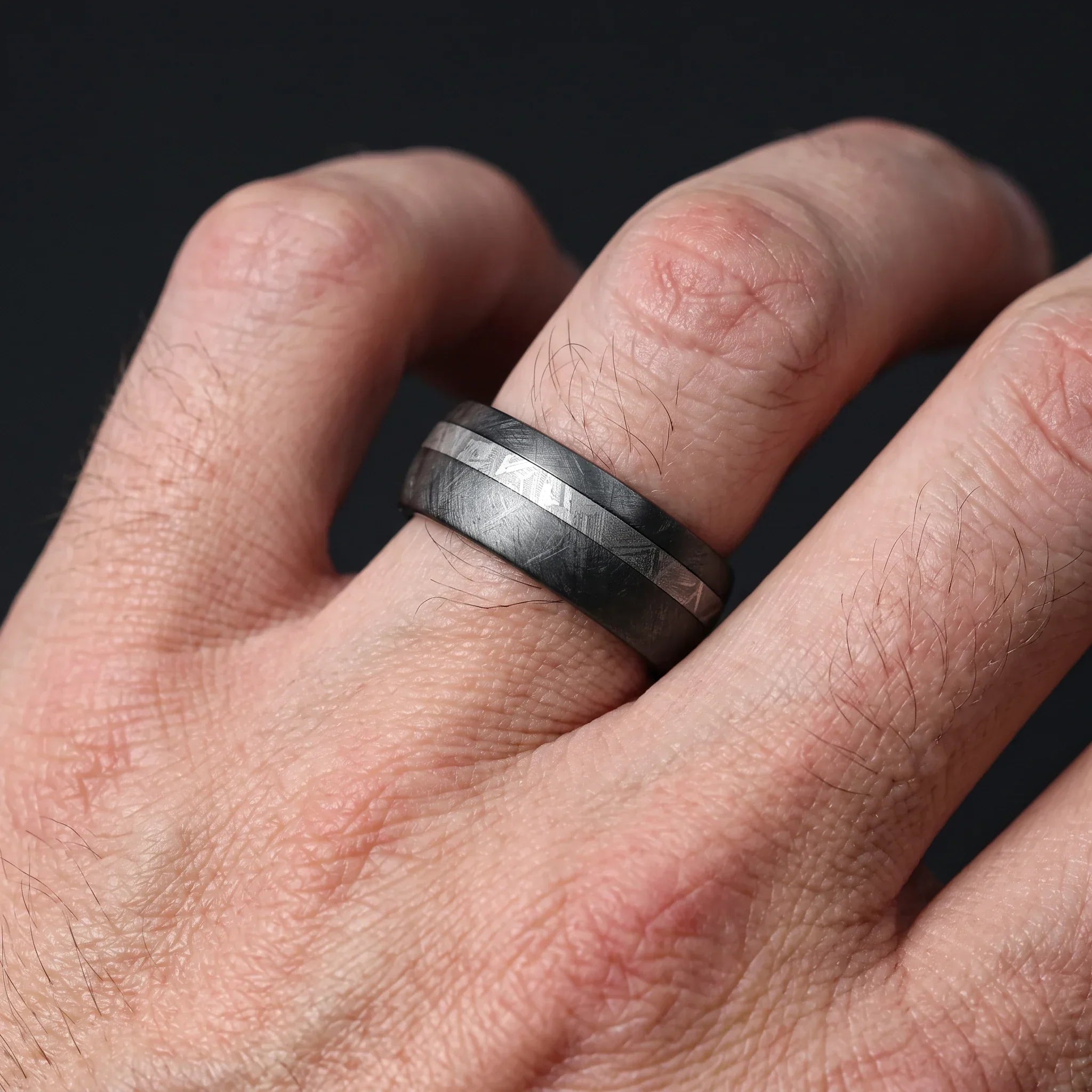 Nyx black zirconium ring with an offset meteorite line, worn on the hand