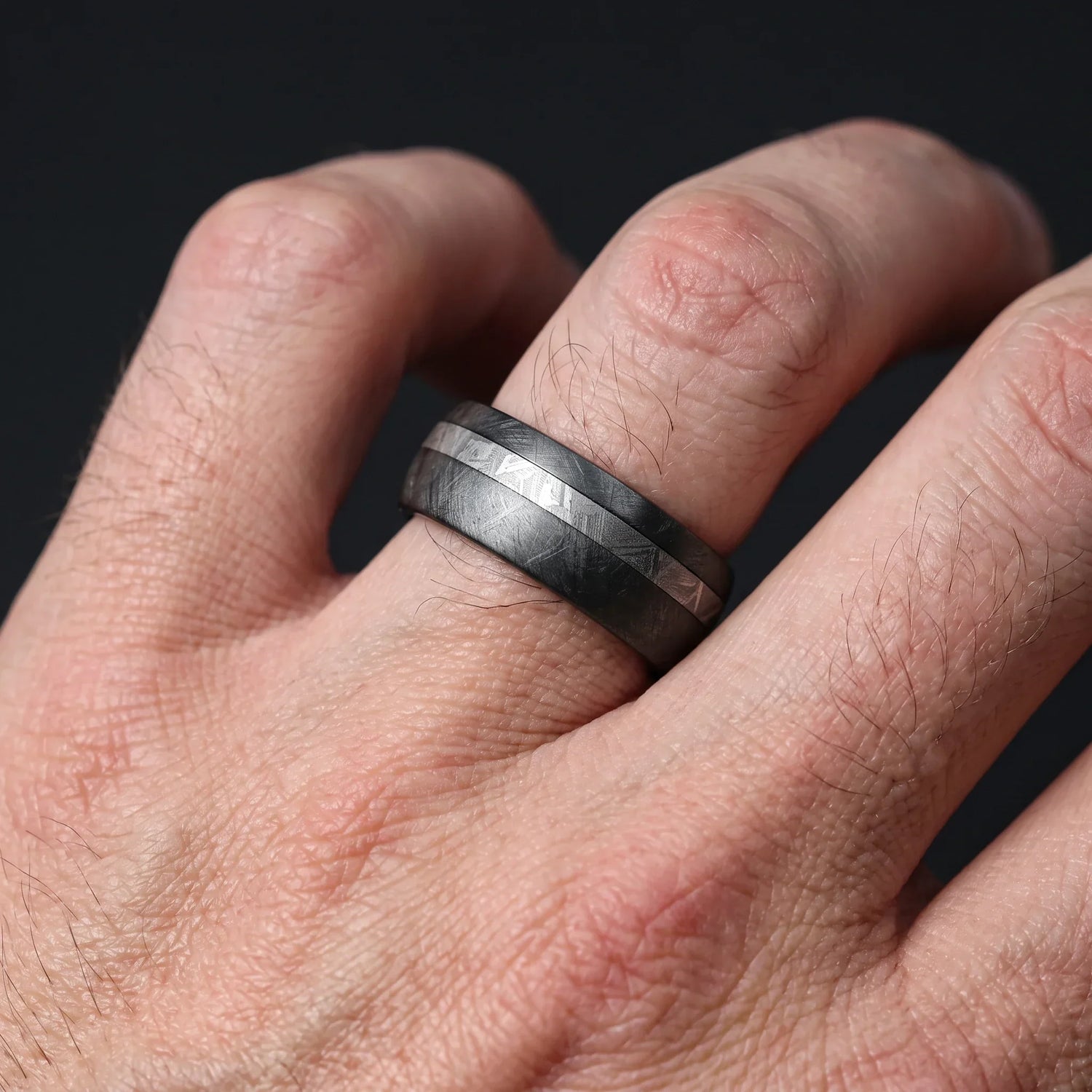Nyx black zirconium ring with an offset meteorite line, worn on the hand